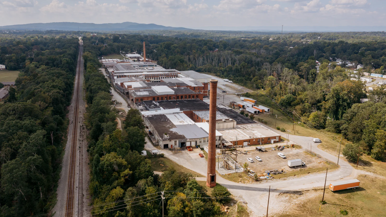 Vista aérea de um complexo industrial com chaminé, cercado por mata e cortado por uma ferrovia