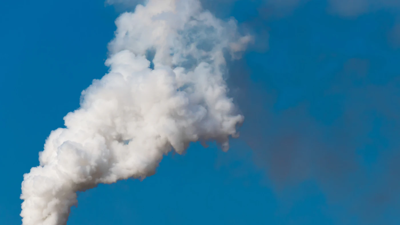 Pluma de vapor e gases saindo da chaminé de uma planta industrial contra o céu azul