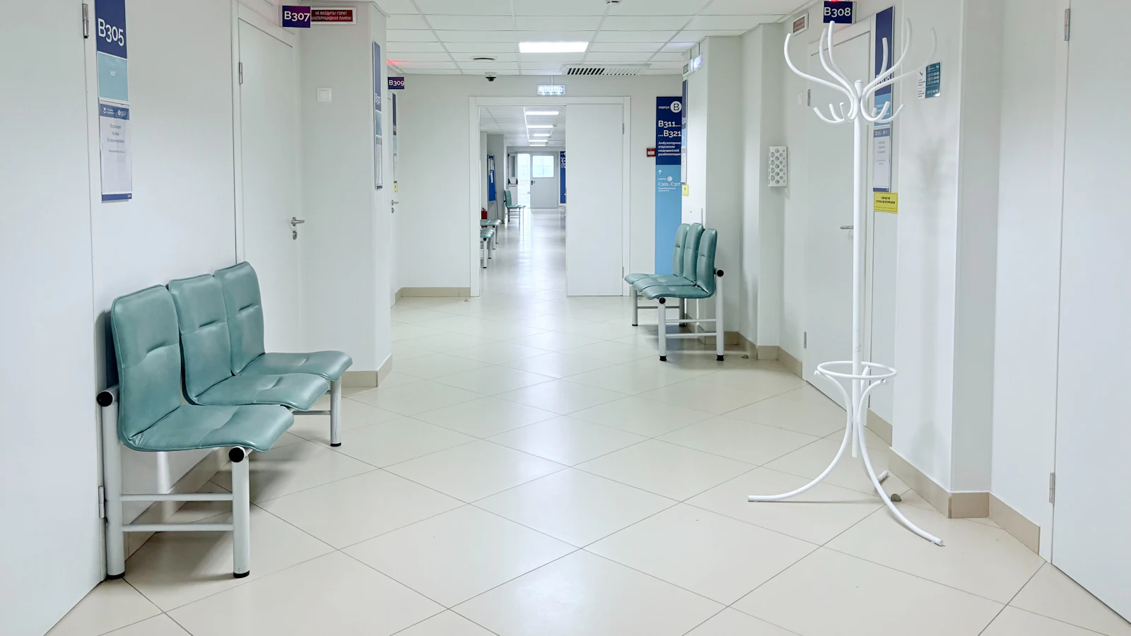 Corredor vazio de hospital com bancos de espera e portas de consultórios