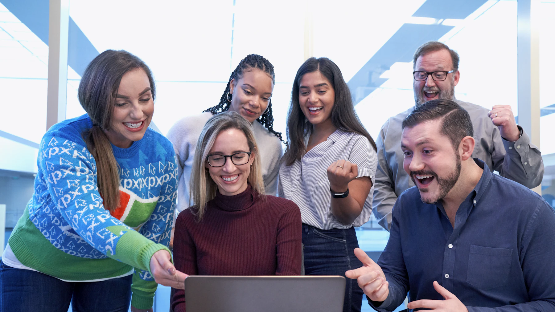 Equipe diversa celebrando um resultado em volta do notebook